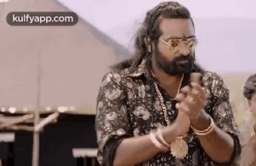 A Man With A Beard And Sunglasses Is Standing In Front Of A Tent And Clapping His Hands . GIF