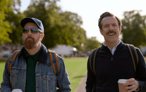 A Man With A Beard And Sunglasses Is Walking With Another Man GIF