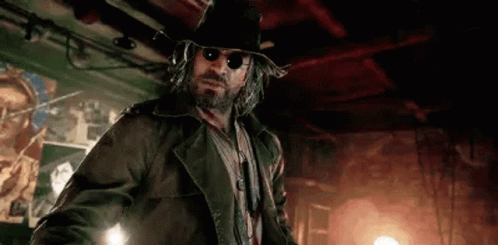 A Man With A Beard And Sunglasses Is Wearing A Hat And A Jacket . GIF
