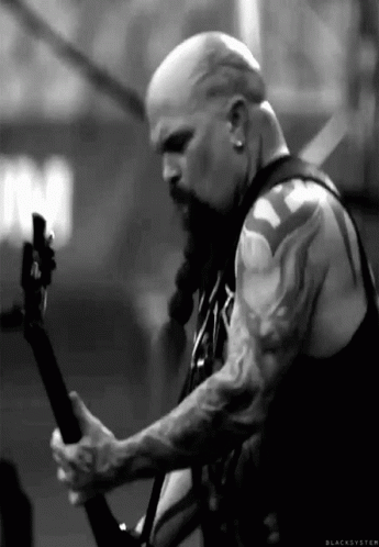 A Man With A Beard And Tattoos Is Playing A Guitar On Stage . GIF