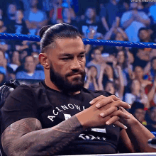 A Man With A Beard And Tattoos Is Sitting In A Chair In A Wrestling Ring . GIF