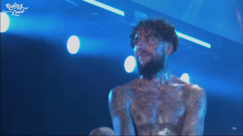 A Man With A Beard And Tattoos On His Chest Is On A Stage With Rolling Loud Written On The Bottom Of The Screen GIF