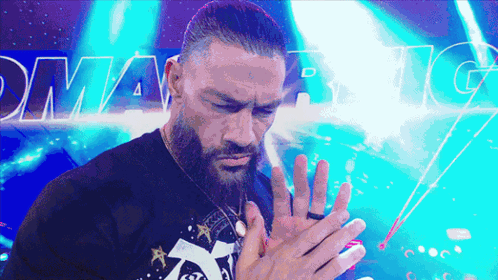 A Man With A Beard Holds His Hands Together In Front Of A Sign That Says Dynamite GIF