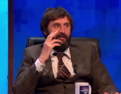 A Man With A Beard In A Suit And Tie Is Sitting In A Chair Talking On A Television Show . GIF