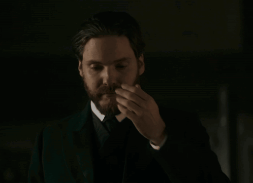 a man with a beard in a suit and tie is smoking a cigarette