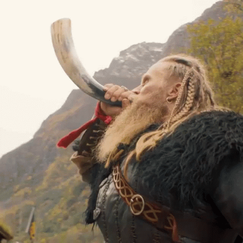 A Man With A Beard Is Blowing A Horn In Front Of Mountains GIF