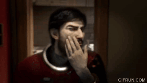 A Man With A Beard Is Covering His Mouth With His Hand In A Room . GIF
