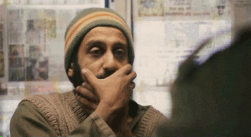 A Man With A Beard Is Covering His Mouth With His Hand While Looking At Another Man . GIF