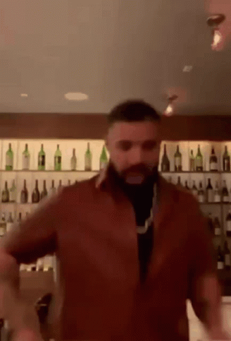 A Man With A Beard Is Dancing In Front Of A Bar Filled With Bottles Of Wine . GIF