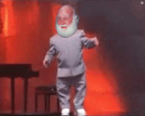 A Man With A Beard Is Dancing On A Stage With A Piano In The Background GIF