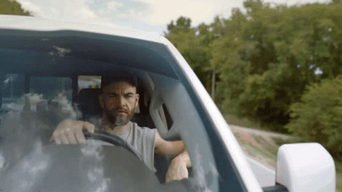 A Man With A Beard Is Driving A Car GIF