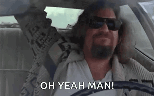 A Man With A Beard Is Driving A Car With His Arms In The Air And Saying `` Oh Yeah Man '' . GIF