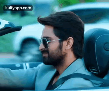A Man With A Beard Is Driving A Convertible Car With Sunglasses On . GIF