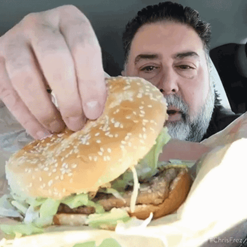 A Man With A Beard Is Eating A Hamburger GIF