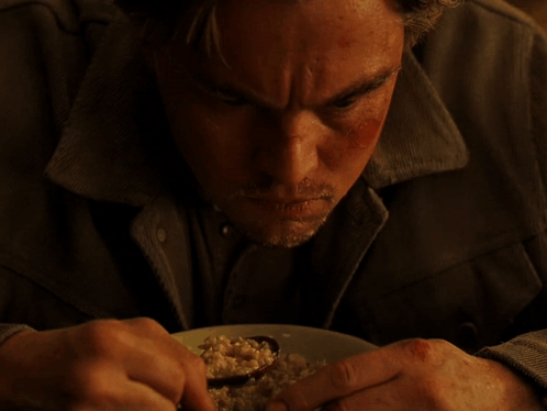 A Man With A Beard Is Eating A Plate Of Food With A Spoon GIF