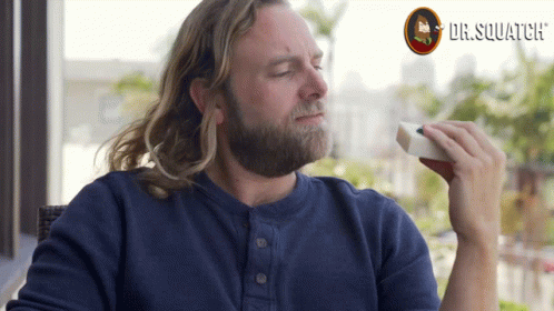 A Man With A Beard Is Eating A Sandwich With Dr. Squatch Written In The Background GIF