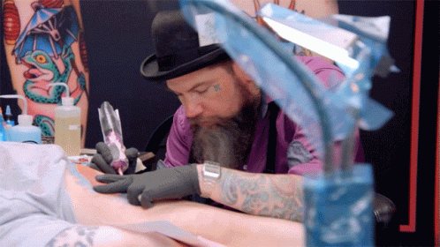 A Man With A Beard Is Getting A Tattoo On A Person 'S Arm GIF
