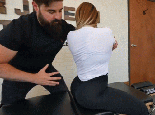 A Man With A Beard Is Helping A Woman With Her Back On A Table GIF