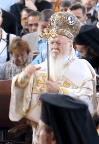 A Man With A Beard Is Holding A Cane In Front Of A Crowd Of People GIF