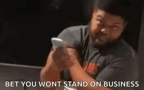 A Man With A Beard Is Holding A Cell Phone In His Hand . GIF