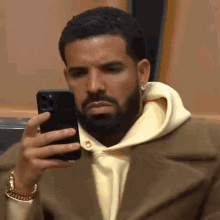 A Man With A Beard Is Holding A Cell Phone In His Hand . GIF