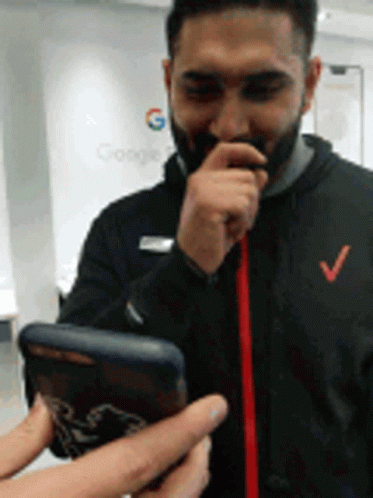 A Man With A Beard Is Holding A Cell Phone With A Google Logo In The Background GIF