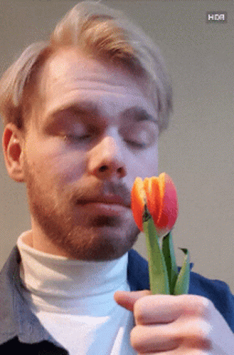 A Man With A Beard Is Holding A Flower In His Hand With A Hdr Button Below It GIF