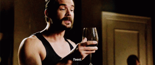 A Man With A Beard Is Holding A Glass Of Wine And Toasting GIF
