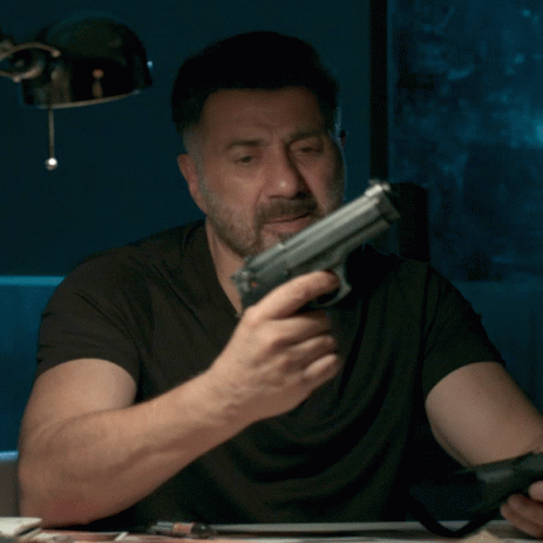 A Man With A Beard Is Holding A Gun In His Right Hand GIF