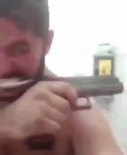 A Man With A Beard Is Holding A Gun In His Right Hand . GIF