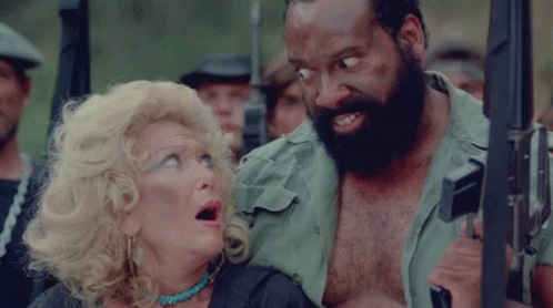 A Man With A Beard Is Holding A Gun Next To A Woman GIF