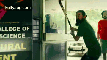 A Man With A Beard Is Holding A Hockey Stick In Front Of A College Of Science Sign GIF