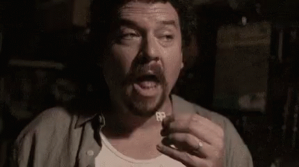 A Man With A Beard Is Holding A Key To His Chest In A Dark Room . GIF