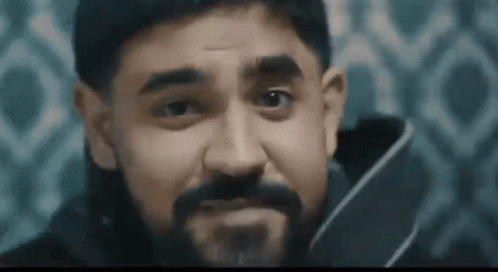 A Man With A Beard Is Holding A Knife In His Hand And Making A Face . GIF