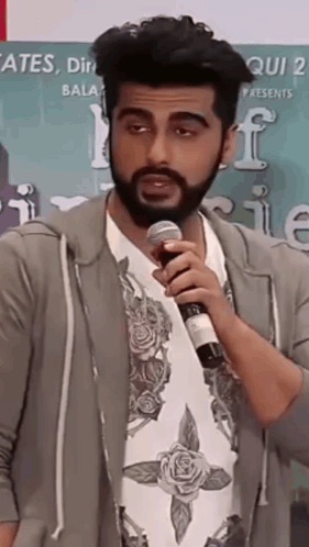 A Man With A Beard Is Holding A Microphone And Talking Into It . GIF