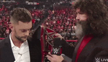 A Man With A Beard Is Holding A Microphone And Talking To Another Man In A Suit . GIF