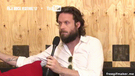 a man with a beard is holding a microphone in front of a sign that says fuji rock festival 17