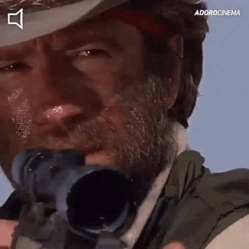 A Man With A Beard Is Holding A Sniper Rifle In Front Of His Face . GIF