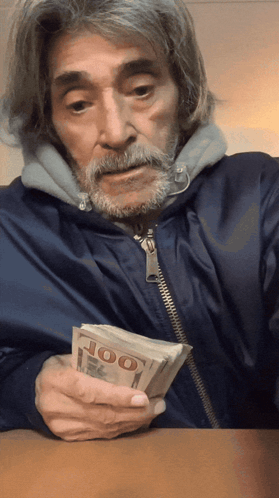 A Man With A Beard Is Holding A Stack Of 100 Dollar Bills GIF