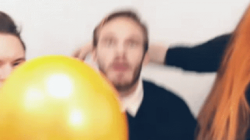 A Man With A Beard Is Holding A Yellow Balloon In Front Of His Face . GIF