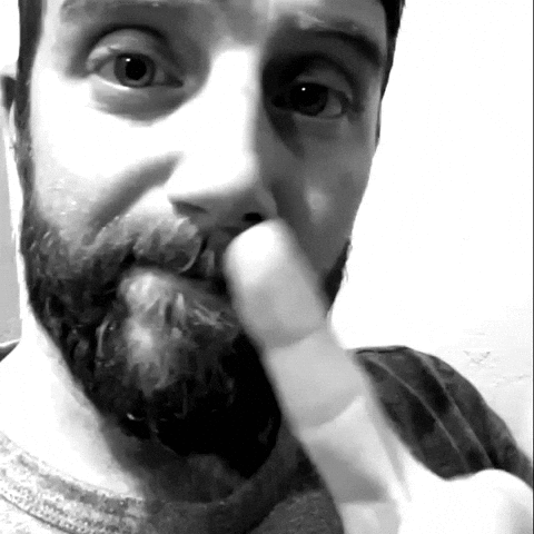 A Man With A Beard Is Holding His Finger To His Nose GIF