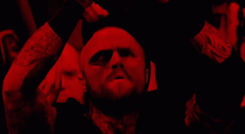 A Man With A Beard Is In A Dark Room With A Red Light Behind Him GIF