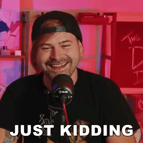 A Man With A Beard Is Laughing In Front Of A Microphone And The Words Just Kidding Are Visible GIF