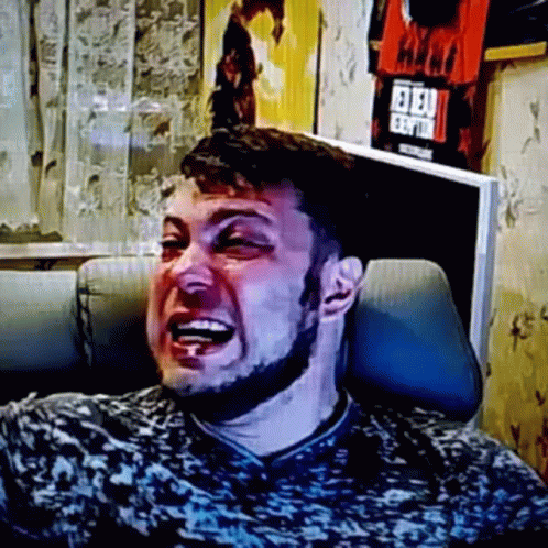 A Man With A Beard Is Laughing While Sitting In A Chair In Front Of A Television . GIF