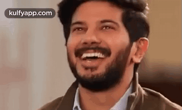 A Man With A Beard Is Laughing With His Mouth Open And His Eyes Closed . GIF