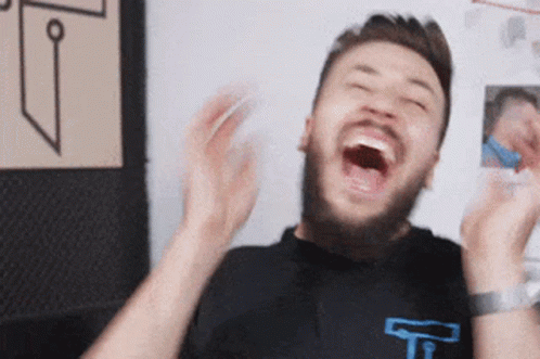 A Man With A Beard Is Laughing With His Mouth Open And His Hands In The Air . GIF