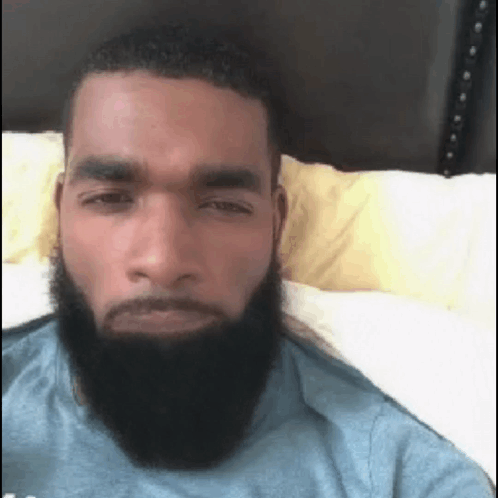 A Man With A Beard Is Laying In Bed And Looking At The Camera . GIF