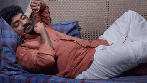 A Man With A Beard Is Laying On A Bed With His Legs Crossed GIF