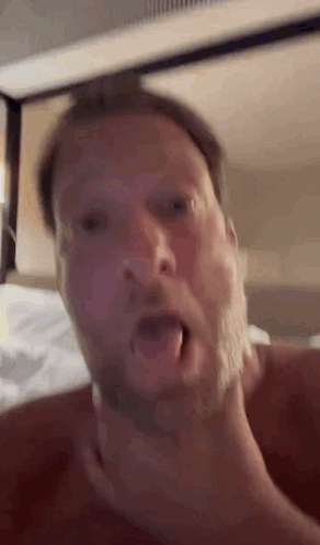A Man With A Beard Is Laying On A Bed With His Mouth Open And His Hand On His Neck . GIF