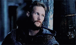 a man with a beard is leaning against a wooden wall in a dark room .